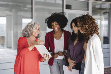 Happy businesswoman with colleagues discussing over tablet PC - JCICF00262