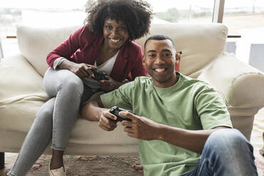 Smiling young woman playing video game with man - JCICF00278