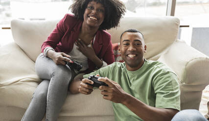 Happy young woman playing video game with man - JCICF00279