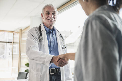 Glücklicher Arzt, der einem Patienten in einer medizinischen Klinik die Hand schüttelt - UUF26636