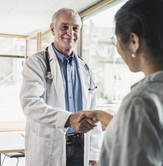 Lächelnder Arzt, der einem Patienten in einer medizinischen Klinik die Hand schüttelt - UUF26637