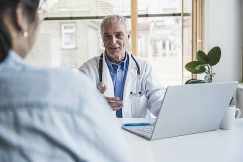 Happy doctor discussing with patient at hospital - UUF26639