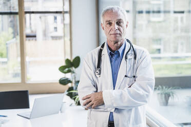 Senior doctor with arms crossed standing in office - UUF26644