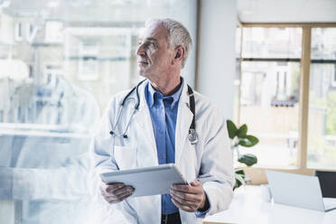 Thoughtful doctor with tablet PC looking through window in office - UUF26651