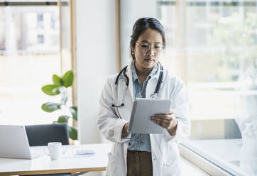 Female doctor using tablet PC by window at hospital - UUF26656