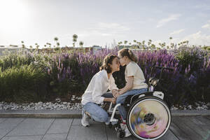 Daughter in wheelchair kissing mother at park - EYAF01984