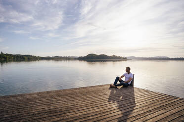 Mature man sitting on pier by lake - DIGF18122