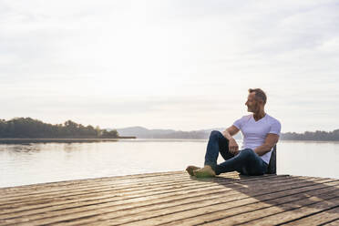 Mature man sitting on jetty at lake - DIGF18123