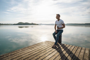 Mature man having coffee sitting on pier by lake - DIGF18130