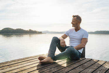 Smiling mature man sitting on jetty - DIGF18155