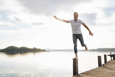 Happy mature man balancing on wooden post of pier - DIGF18180