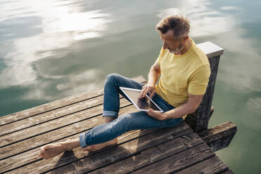 Älterer Mann mit Tablet-PC auf dem Pier über dem See sitzend - DIGF18184