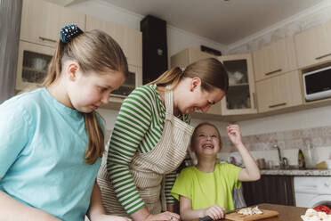 Glückliches Mädchen mit Mutter und Schwester bei der Zubereitung von Essen in der Küche zu Hause - OSF00174