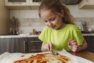 Mädchen, das Tomatensauce auf Pizzateig streicht - OSF00176