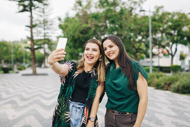 Happy friends taking selfie through smart phone in park - DCRF01250