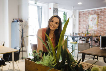 Happy businesswoman seen through plants in office - DCRF01262
