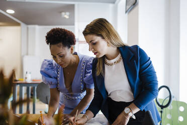 Businesswoman writing notes with colleague in office - DCRF01265