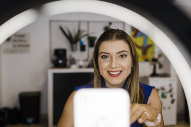 Lächelnde junge Geschäftsfrau beim Vloggen im Büro - DCRF01281