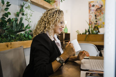 Geschäftsfrau mit Kaffeebecher und Laptop im Büro - DCRF01293