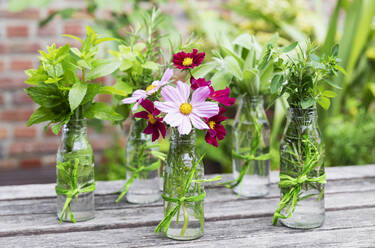 Frische Kräuter und Blumen in dekorierten Glasflaschen stehen auf dem Balkontisch - GWF07475