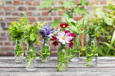 Frische Kräuter und Blumen in dekorierten Glasflaschen stehen auf dem Balkontisch - GWF07476