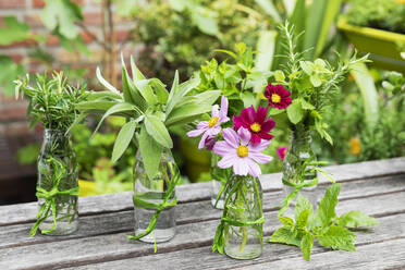 Frische Kräuter und Blumen in dekorierten Glasflaschen stehen auf dem Balkontisch - GWF07477