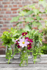 Frische Kräuter und Blumen in dekorierten Glasflaschen stehen auf dem Balkontisch - GWF07478