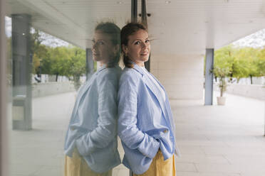 Businesswoman with hand in pocket leaning on window - JRVF02975