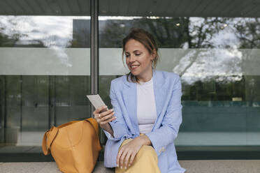 Lächelnde Geschäftsfrau, die vor einem Glasfenster sitzt und telefoniert - JRVF02980