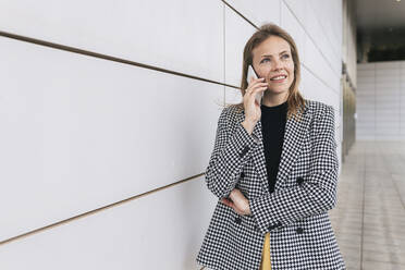 Lächelnde Geschäftsfrau, die an der Wand stehend telefoniert - JRVF02983