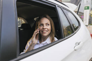 Lächelnde Geschäftsfrau, die am Telefon spricht und durch ein Autofenster schaut - JRVF02996