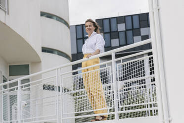 Smiling businesswoman standing by railing on footbridge - JRVF03005