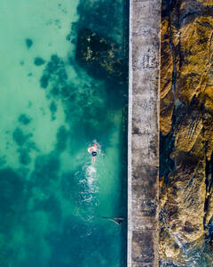Luftaufnahme einer Person beim Schwimmen im Gezeitenbecken von Camps Bay, Kapstadt, Südafrika. - AAEF14715