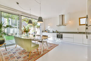Lampen hängen über einem Esstisch mit Stühlen und einer Couch in einer modernen geräumigen Küche mit weißen Möbeln und Chromgeräten in einem modernen Haus - ADSF35520