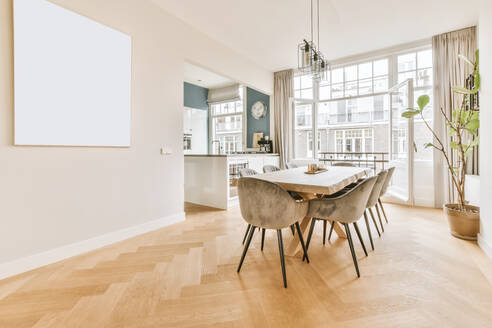 Long table and comfortable chairs located in dining room near kitchen against opened balcony door in daytime in modern apartment - ADSF35553