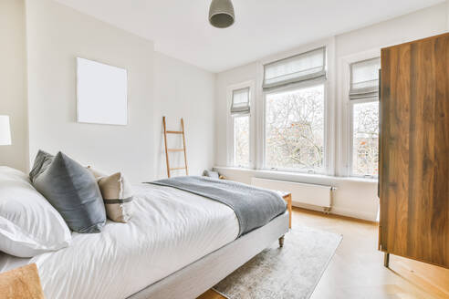Breites bequemes Bett mit warmen Decken und weichen Kissen im trendigen Schlafzimmer der modernen Wohnung - ADSF35557