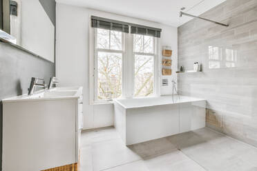 Interior of light contemporary bathroom with bathtub and sinks against window in daytime at home - ADSF35560