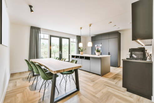 Contemporary table and chairs placed near kitchen furniture against glass door and windows in light room at home - ADSF35579