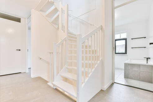 White staircase with railings located in corridor near bathroom with opened door in daytime at home - ADSF35588