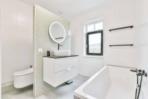 Schubladen mit Waschbecken und Spiegel an der Trennwand zwischen Toilette und Badewanne in einem sonnendurchfluteten Badezimmer zu Hause - ADSF35589