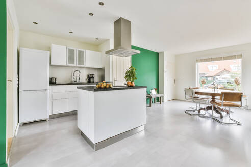 Contemporary kitchen interior with white furniture and comfortable chairs at round round dining table in daylight - ADSF35603