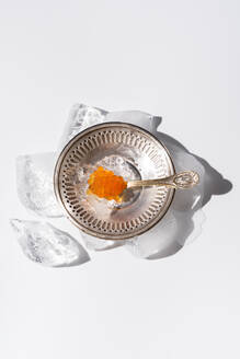 From above orange tobiko caviar served on silver plate with ice with spoon on white background - ADSF35609