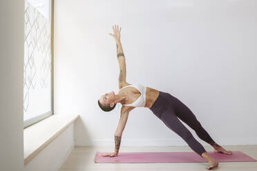 Woman practicing yoga on exercise mat in front of wall - MTBF01217