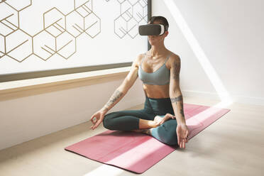 Frau übt Lotussitz auf Matte mit Virtual-Reality-Headset im Studio - MTBF01222
