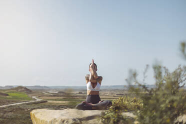 Woman practicing Garudasana sitting on rock at Bardenas Reales in Spain - MTBF01232