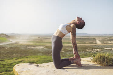 Woman doing stretching exercise on rock at Bardenas Reales in Spain - MTBF01233