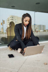 Young businesswoman using laptop in front of glass wall - JRVF03025