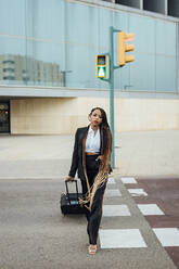Junge Geschäftsfrau mit Koffer beim Überqueren der Straße - JRVF03026