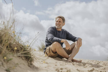 Happy mature man sitting on sand - MFF09176