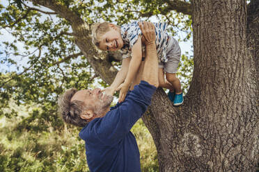 Happy father playing with son by tree - MFF09180